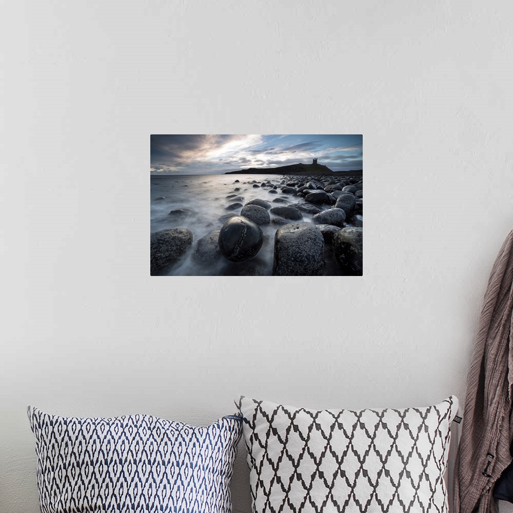 A bohemian room featuring View at sunrise towards the ruin of Dunstanburgh Castle from the beach of basalt boulders known a...