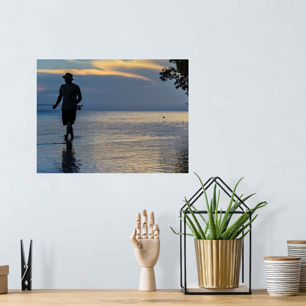 A bohemian room featuring A silhouetted man fly fishing on the beach in Belize at sunset.