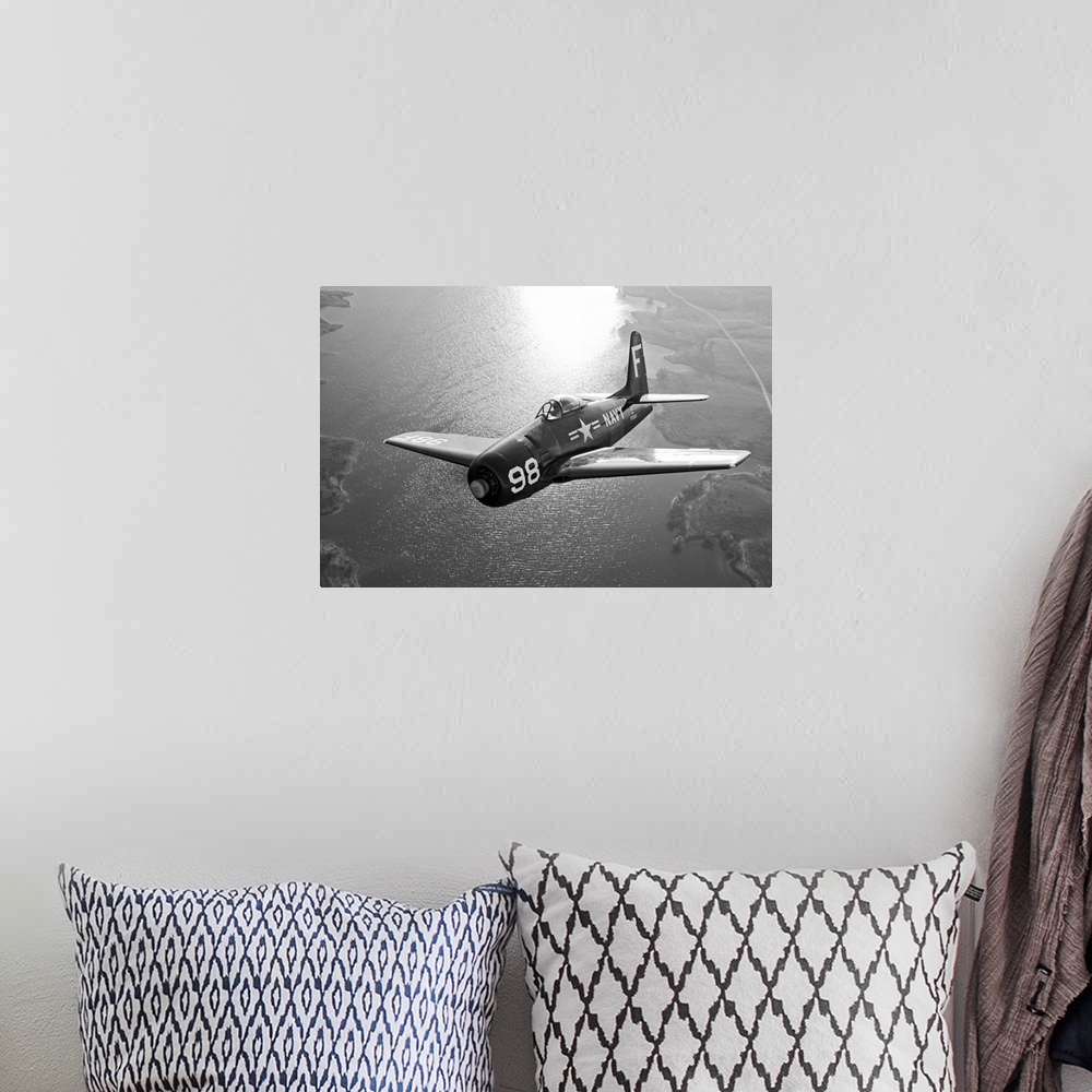 A bohemian room featuring A vintage military aircraft is photographed in black and white as it flies over a large body of w...