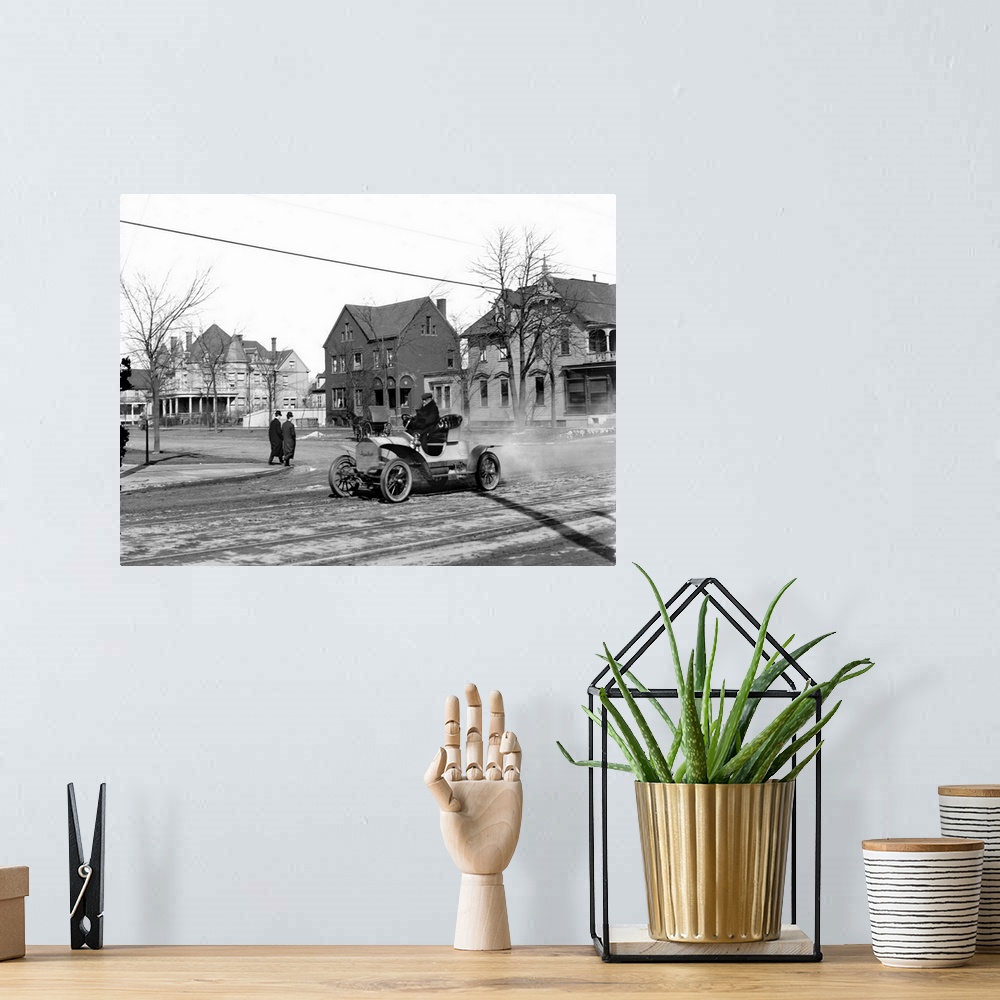 A bohemian room featuring Man driving an automobile through an American town. Photograph, c1905.