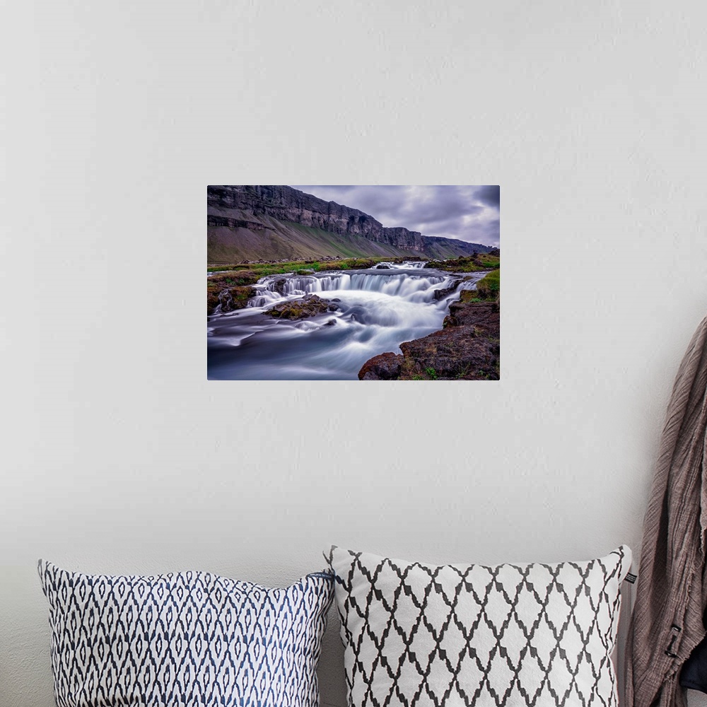 A bohemian room featuring Rushing water in a freezing river under a cloudy sky in Iceland.
