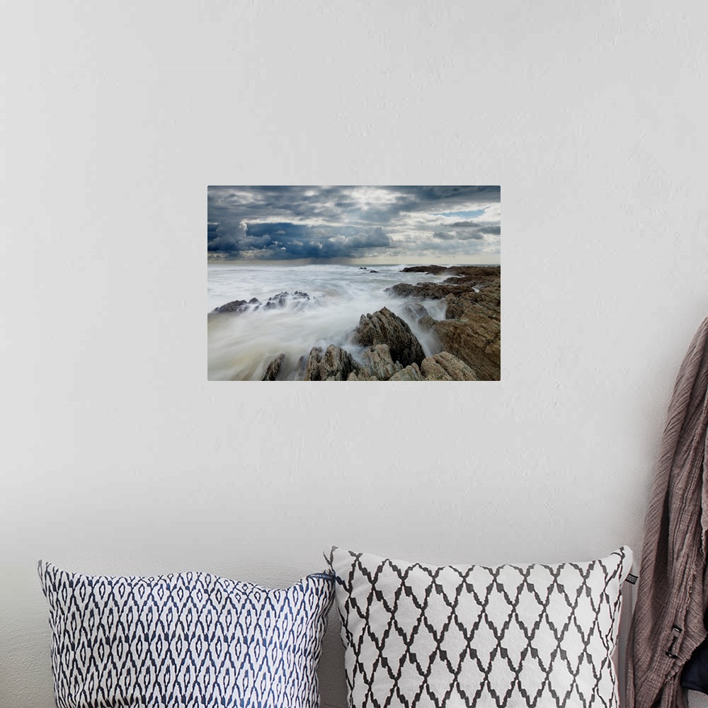 A bohemian room featuring Jagged rocks on coastline with white surf under grey storm clouds