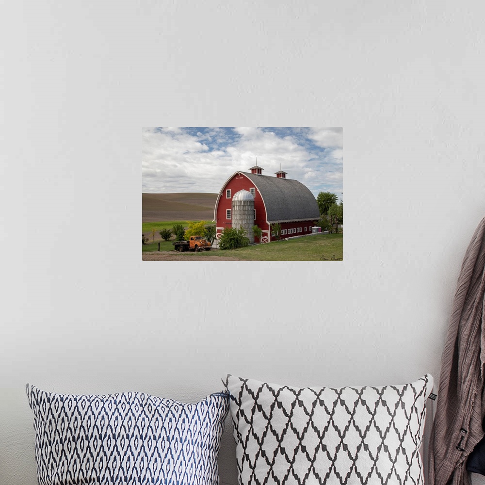A bohemian room featuring A photograph of a large red barn and grain silo with a vintage orange truck parked out front
