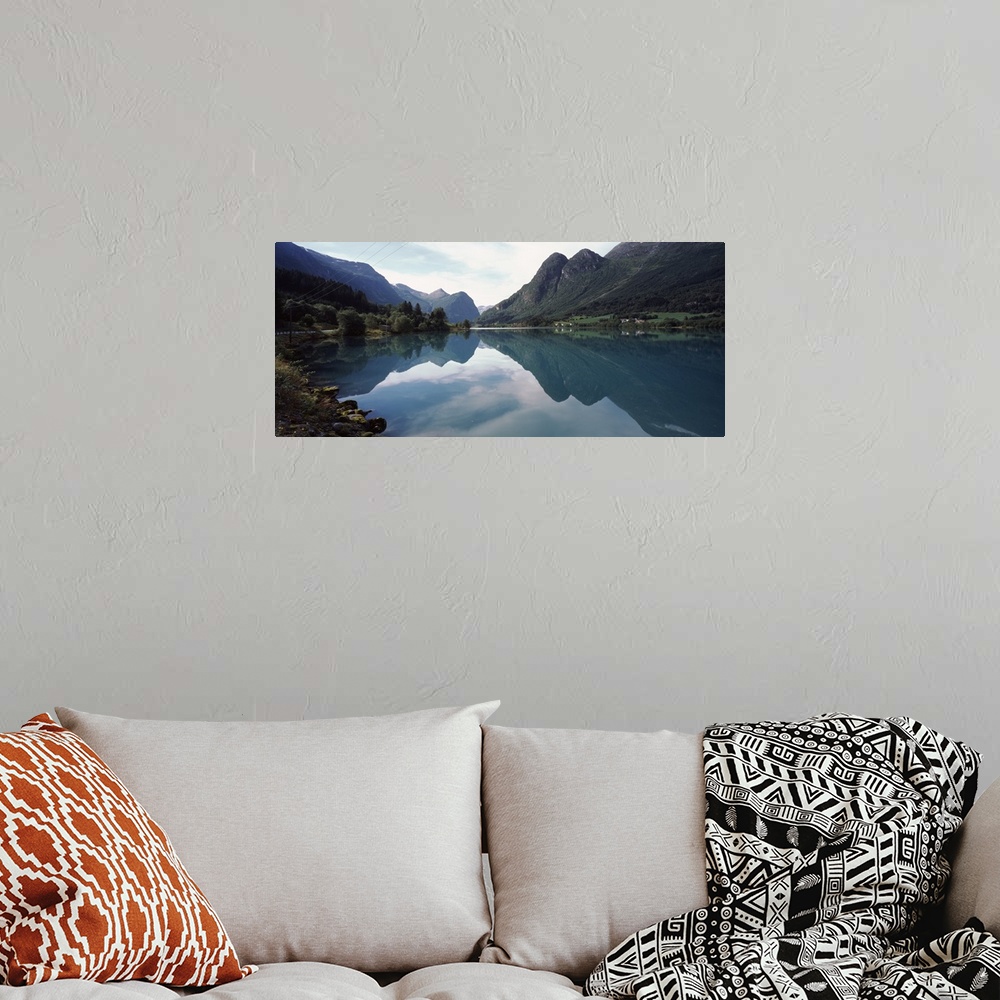 A bohemian room featuring A large piece that is a photograph of mountains lining a body of water that reflect in the still ...