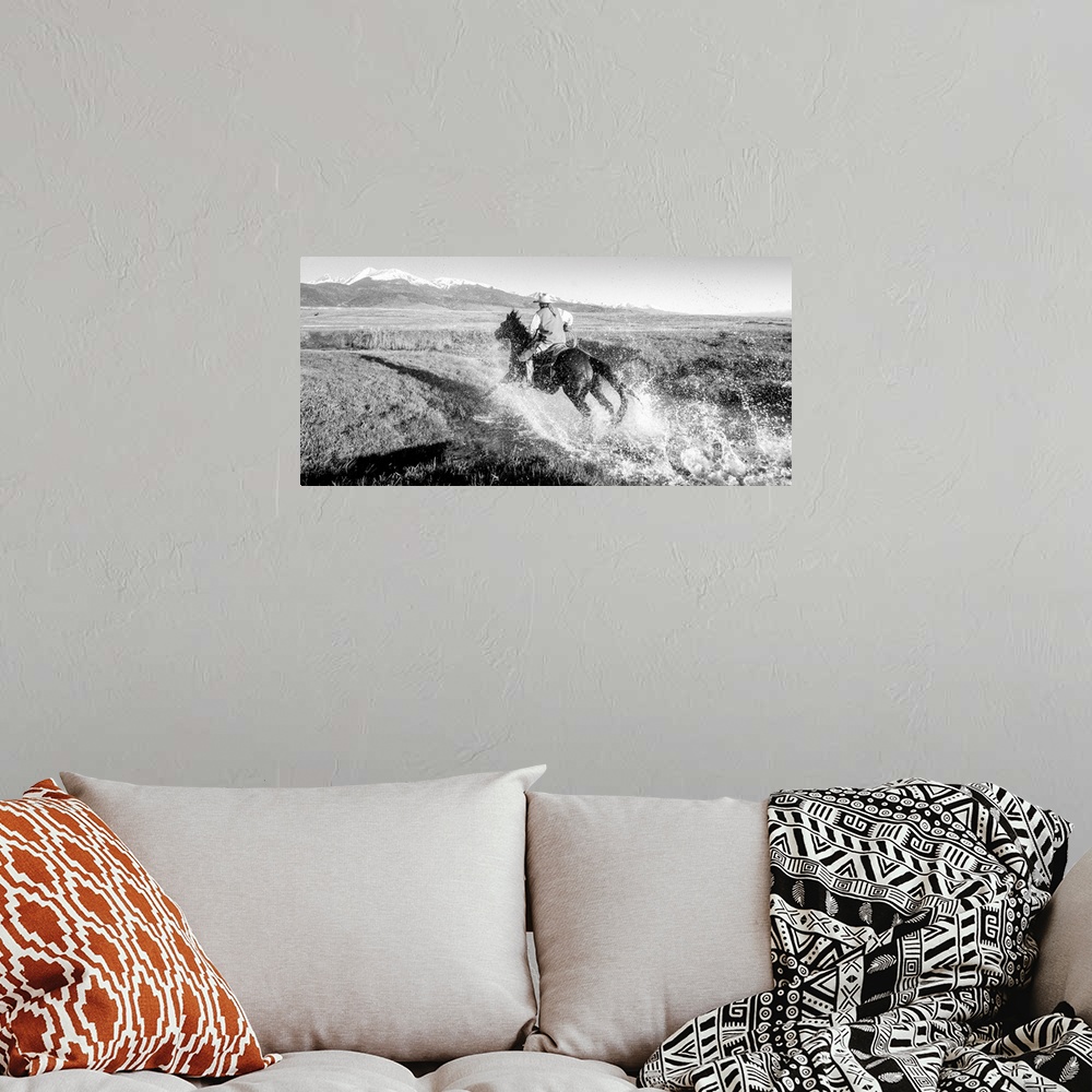 A bohemian room featuring Action photograph of a cowgirl splashing across a river on horseback with snow capped mountains i...