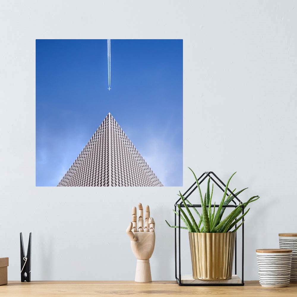 A bohemian room featuring Looking up at the top of a skyscraper with an airplane leaving a vapor trail behind him.