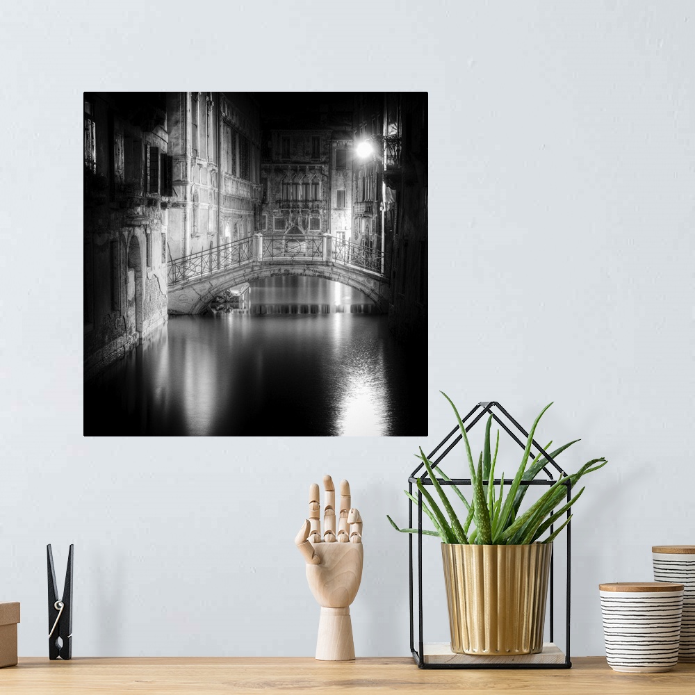 A bohemian room featuring High contrast black and white image of a bridge in a canal in the center of a city at night.