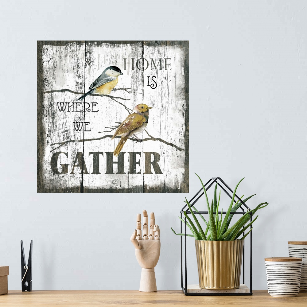 A bohemian room featuring A decorative painting of two birds sitting on branches and the text ?Home is Where We Gather? pai...