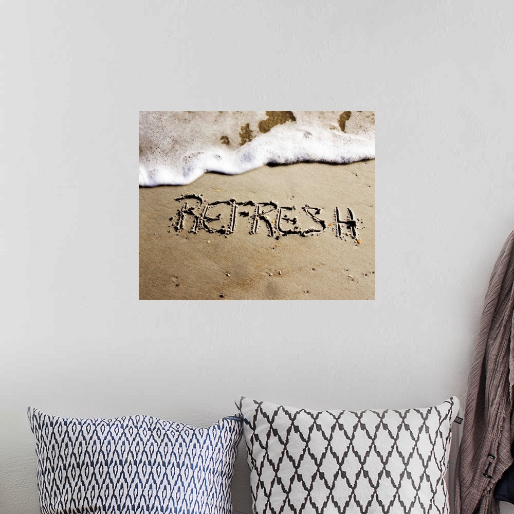 A bohemian room featuring The word "Refresh" drawn in the sand near the ocean water.