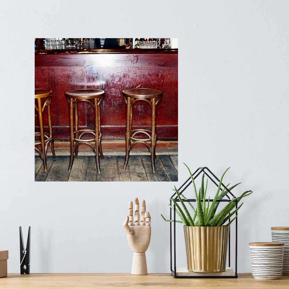 A bohemian room featuring Three tall stools are photographed sitting in front of an empty bar.