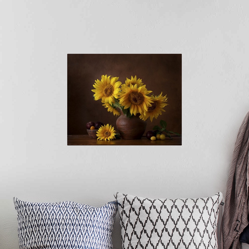 A bohemian room featuring Bouquet of sunflowers in old clay jug with ripe cherry plum branches in the foreground.