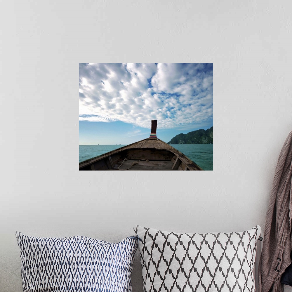 A bohemian room featuring Long boat in sea with cloudy sky and mountain in background.