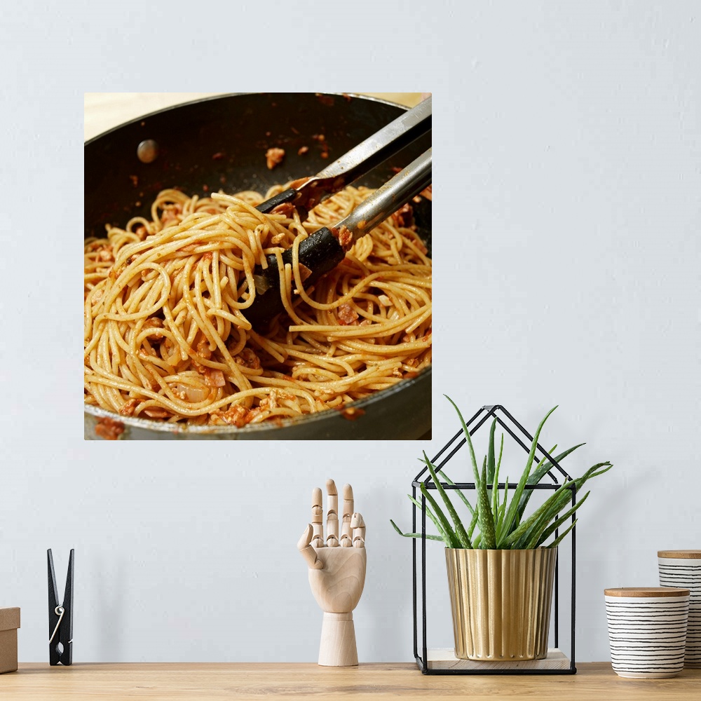 A bohemian room featuring Tongs tossing spaghetti with meat sauce in pan