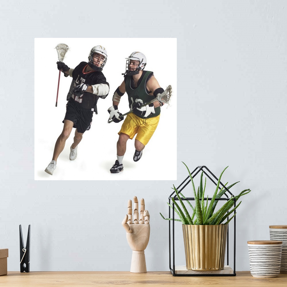 A bohemian room featuring two caucasian male lacrosse players from opposite teams run as the one in the green jersey tries ...