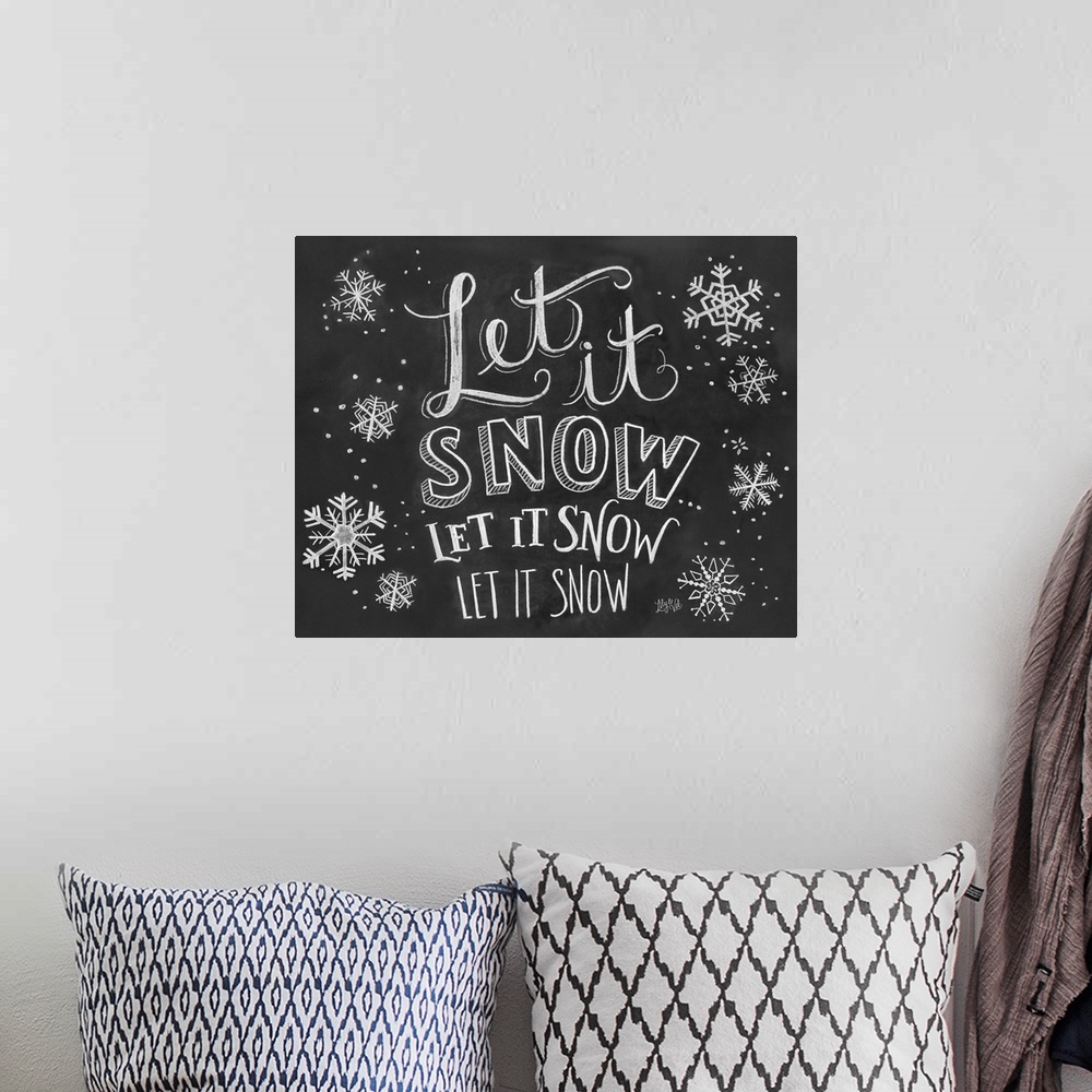 A bohemian room featuring "Let it snow" handwritten with several snowflakes in white chalk on a black background.