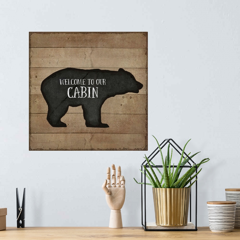 A bohemian room featuring "Welcome to Our Cabin" on a bear silhouette over a wooden background.