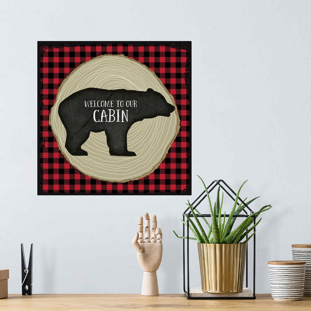 A bohemian room featuring "Welcome to Our Cabin" on a bear silhouette over red and black plaid and tree rings.