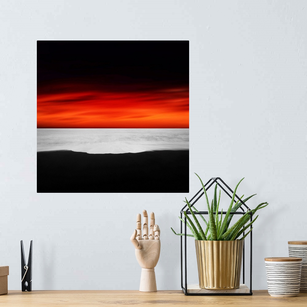 A bohemian room featuring A dramatic photograph of a blazing sky hanging over a white seascape seen from a black sand beach.