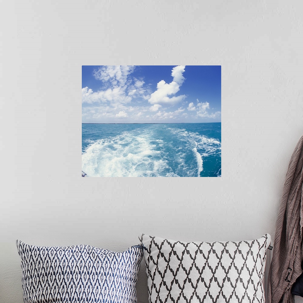 A bohemian room featuring Photo on canvas of the ocean with land in the far distance and puffy clouds above looking from be...