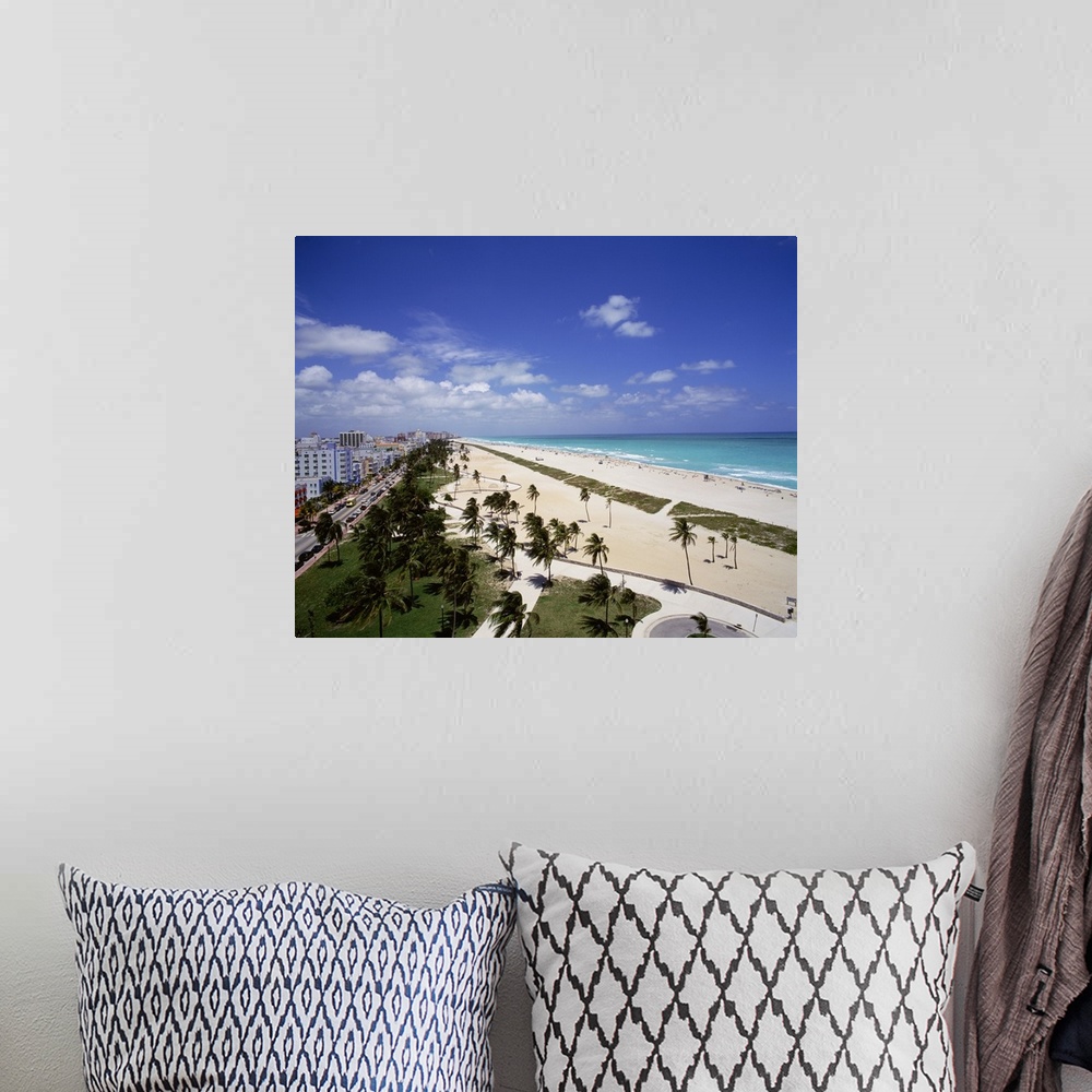 A bohemian room featuring Canvas photo art of a city and street on the left meeting white sand and ocean on the right with ...