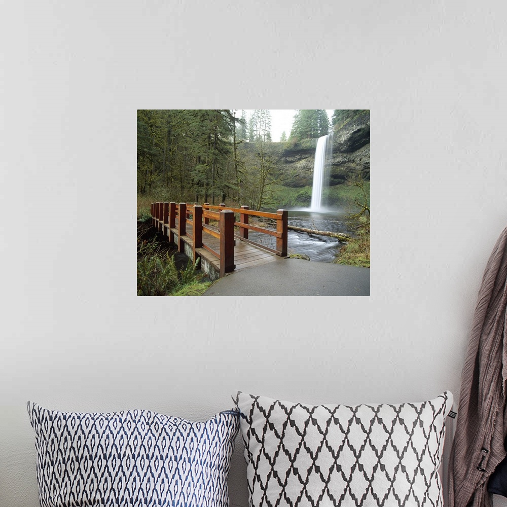 A bohemian room featuring Large wall docor of a wooden bridge going across a river with a thin waterfall on the right.