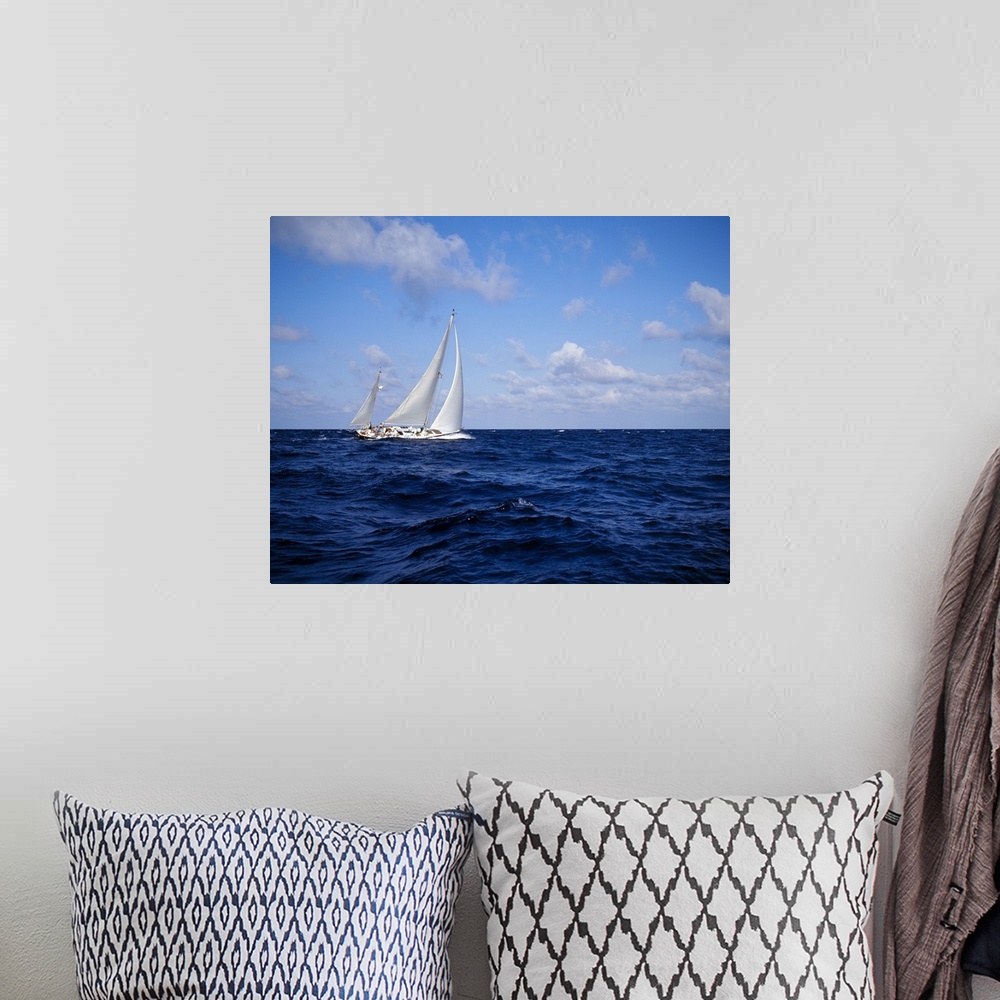 A bohemian room featuring A single sail boat is photographed on rough ocean water with a cloudy sky above.