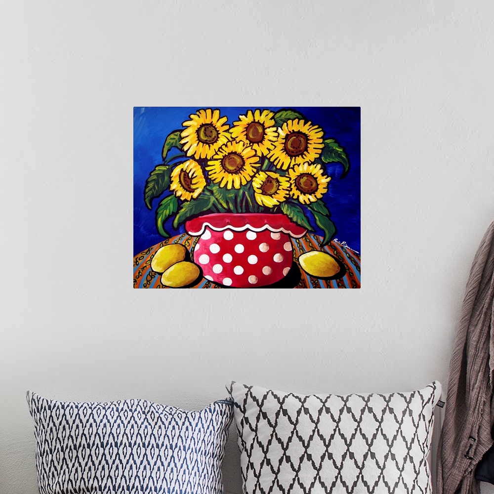 A bohemian room featuring Fun and colorful red polka dotted vase filled with sunflowers. Three lemons sit along side.