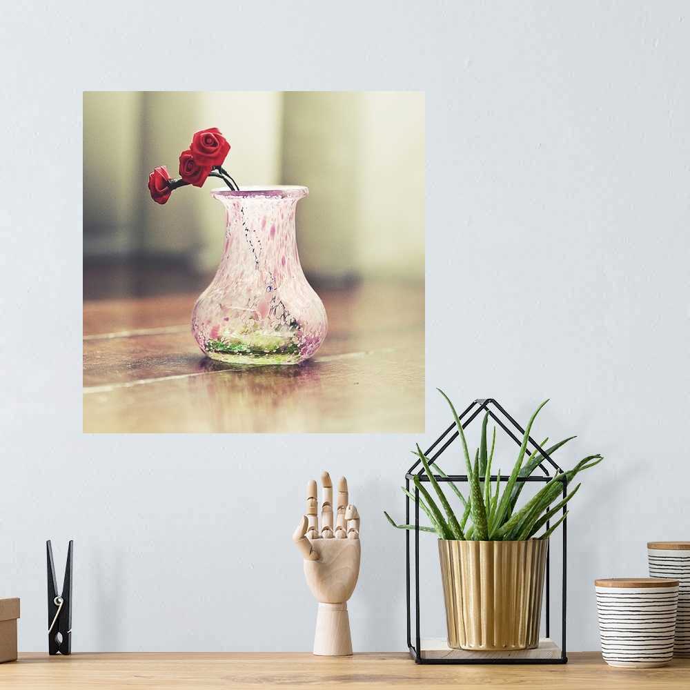 A bohemian room featuring Close up of a decorated small pink pitcher with three red roses made of cloth inside.