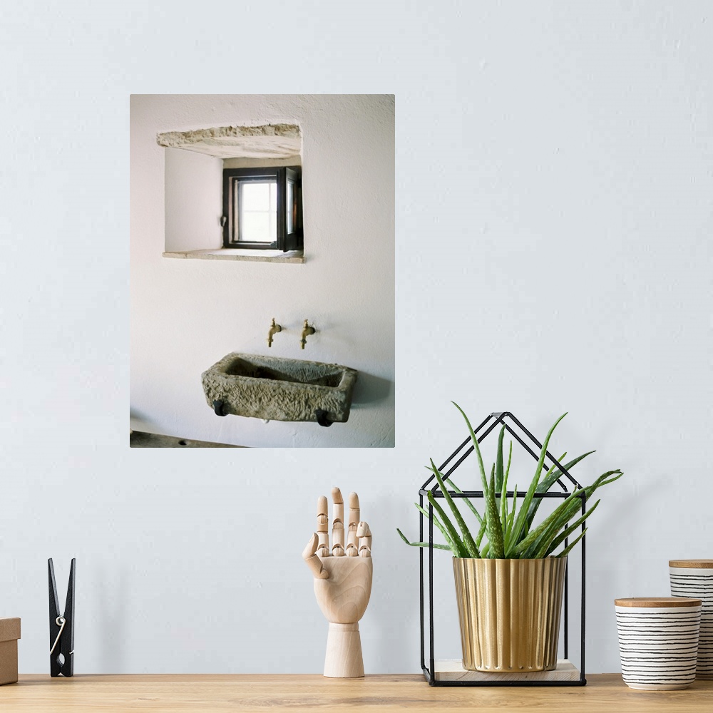 A bohemian room featuring A photograph of a rustic stone wall basin underneath a small window in a white stucco mediterrane...