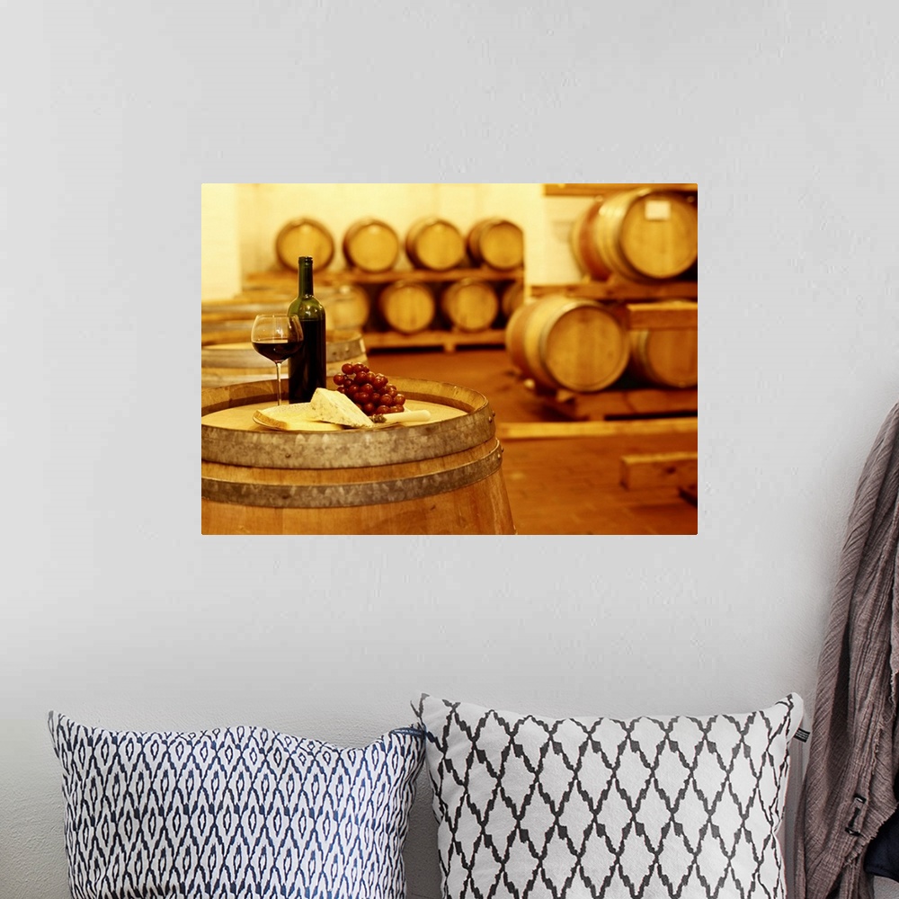 A bohemian room featuring A photograph in a wine cellar of an upright barrel with a glass of wine, grapes, and cheese sitti...