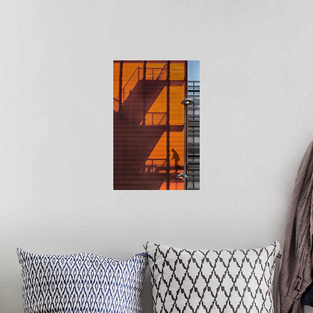A bohemian room featuring Shadow of a fire escape staircase and a person walking down cast onto the side of an orange build...