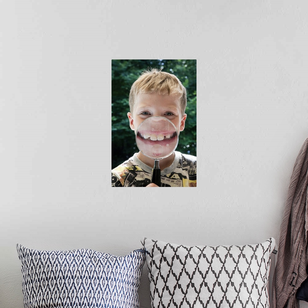 A bohemian room featuring blond boy behind magnifying glass smiling