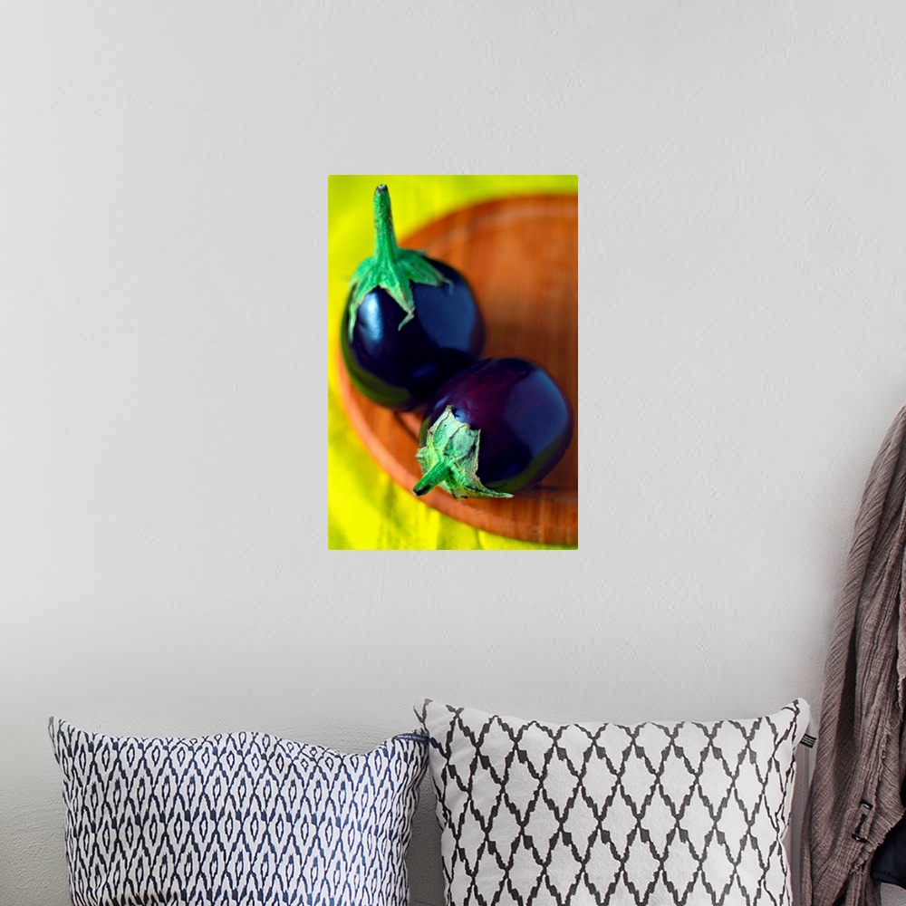 A bohemian room featuring Close-up of two tiny round eggplants (Solanum melongena) on round wooden chopping board and brigh...