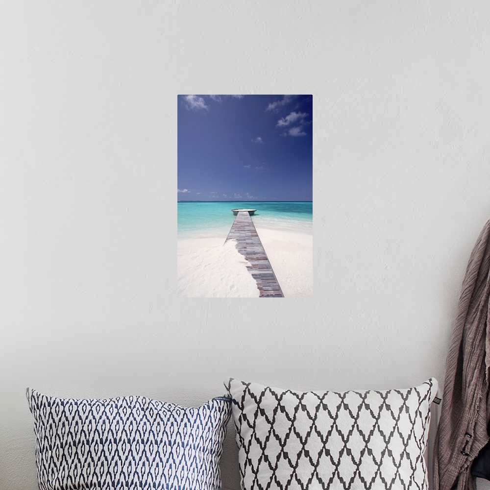 A bohemian room featuring Vertical photo of a wooden walkway stretching out into the tropical sea, partly covered in sand.