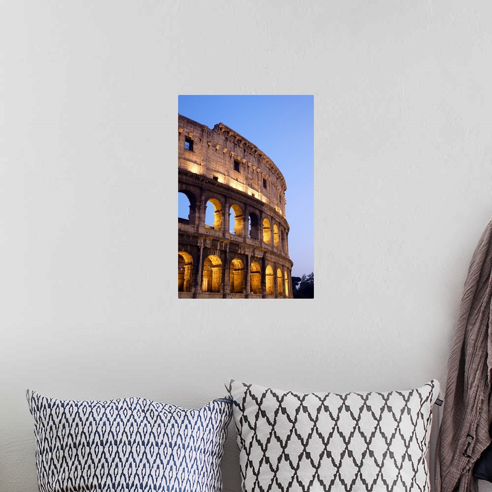 A bohemian room featuring Veridical photograph of the Roman Coliseum at dusk with the lights illuminating the arched windows.