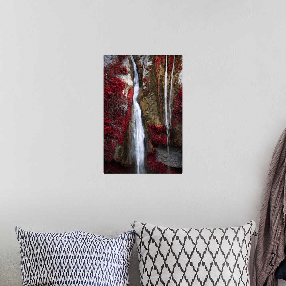 A bohemian room featuring A photograph of a thin waterfall running through cracked rocks and fall foliage.