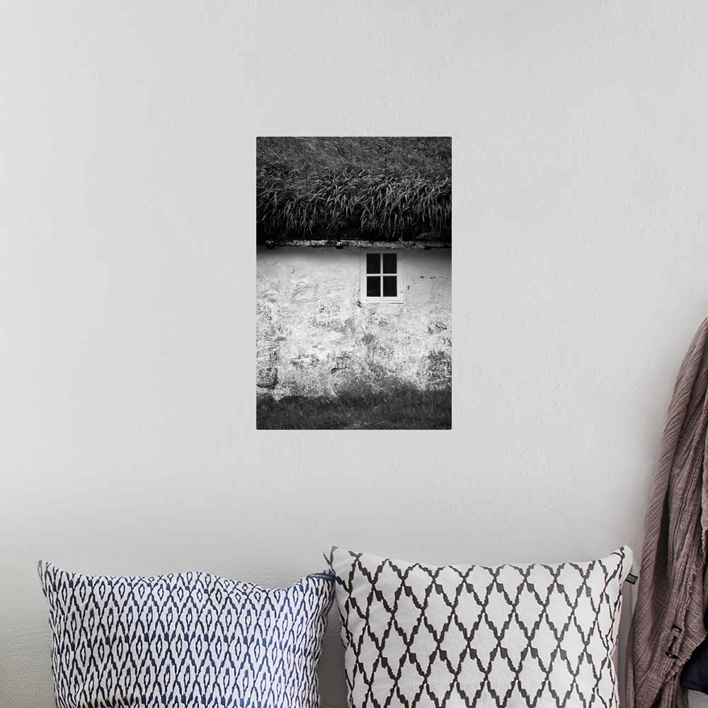 A bohemian room featuring Black and white image of a small window in the stone wall of a house with a grassy roof.