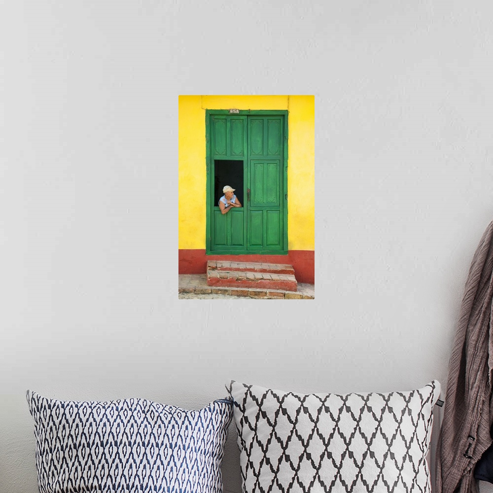 A bohemian room featuring Photograph of a man leaning through a window connected to a large green door on a yellow and red ...