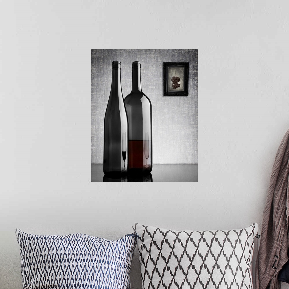 A bohemian room featuring Two glass wine bottles with reflections of glasses on them, and a framed image of grapes on the w...