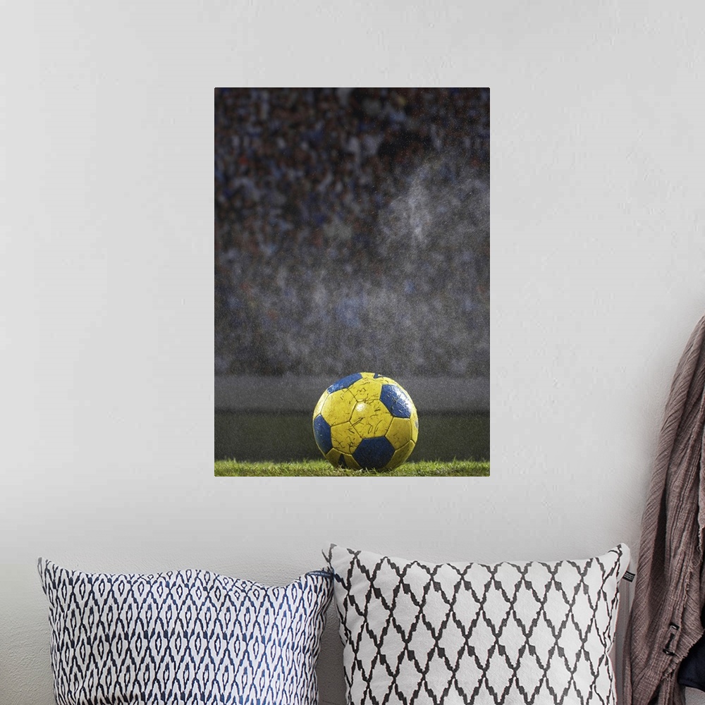 A bohemian room featuring A soccer ball that is covered with wet grass is photographed sitting on a field with the crowd ou...