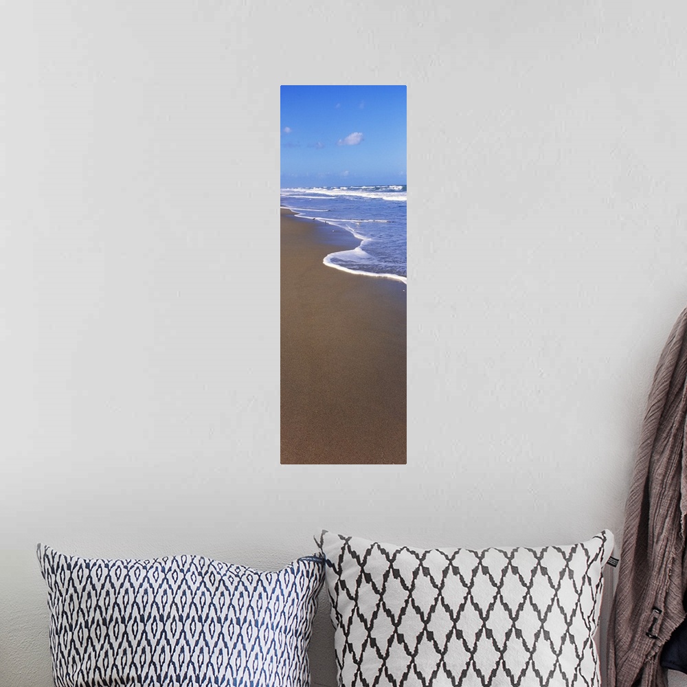A bohemian room featuring A tall panoramic piece of the ocean water rushing up onto the dark sand.