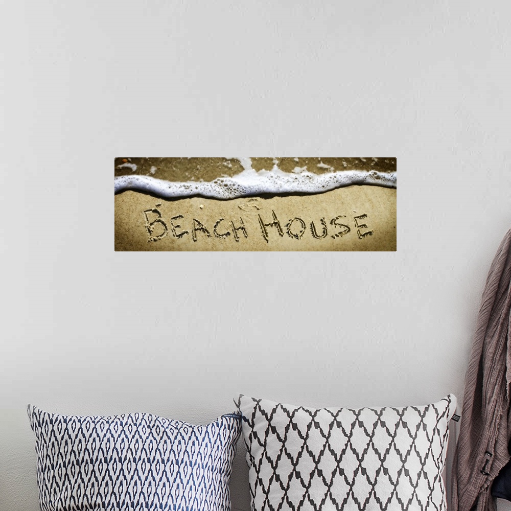 A bohemian room featuring The word "Beach House" drawn in the sand near the ocean water.