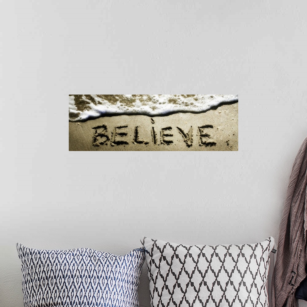 A bohemian room featuring The word "Believe" drawn in the sand near the ocean water.