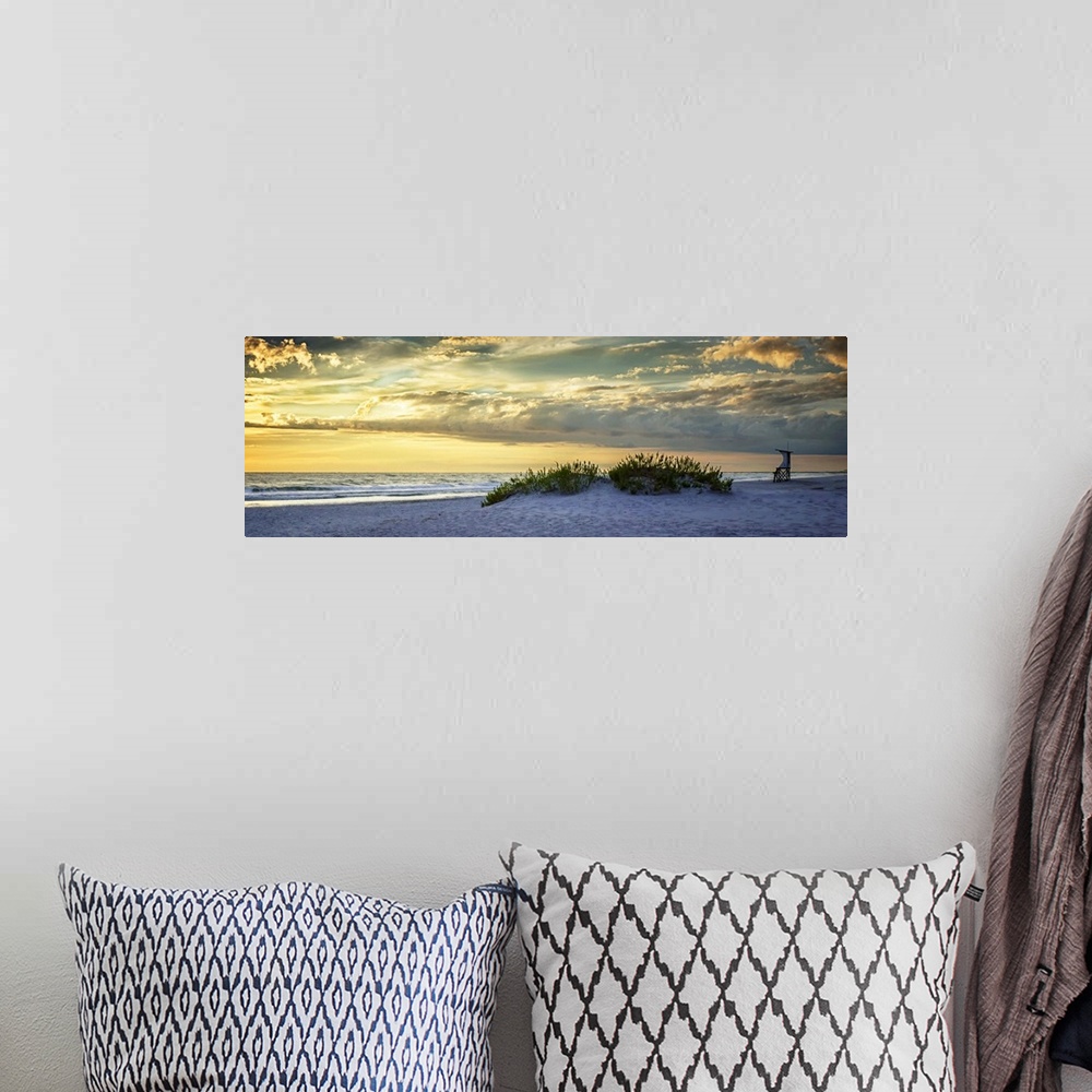 A bohemian room featuring Cloudy sky at sunrise glowing yellow over the beach.