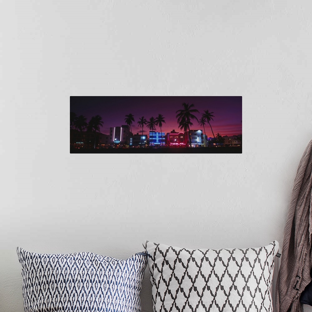 A bohemian room featuring A panoramic canvas of neon lights on art deco buildings on the shore front lined with palm trees.