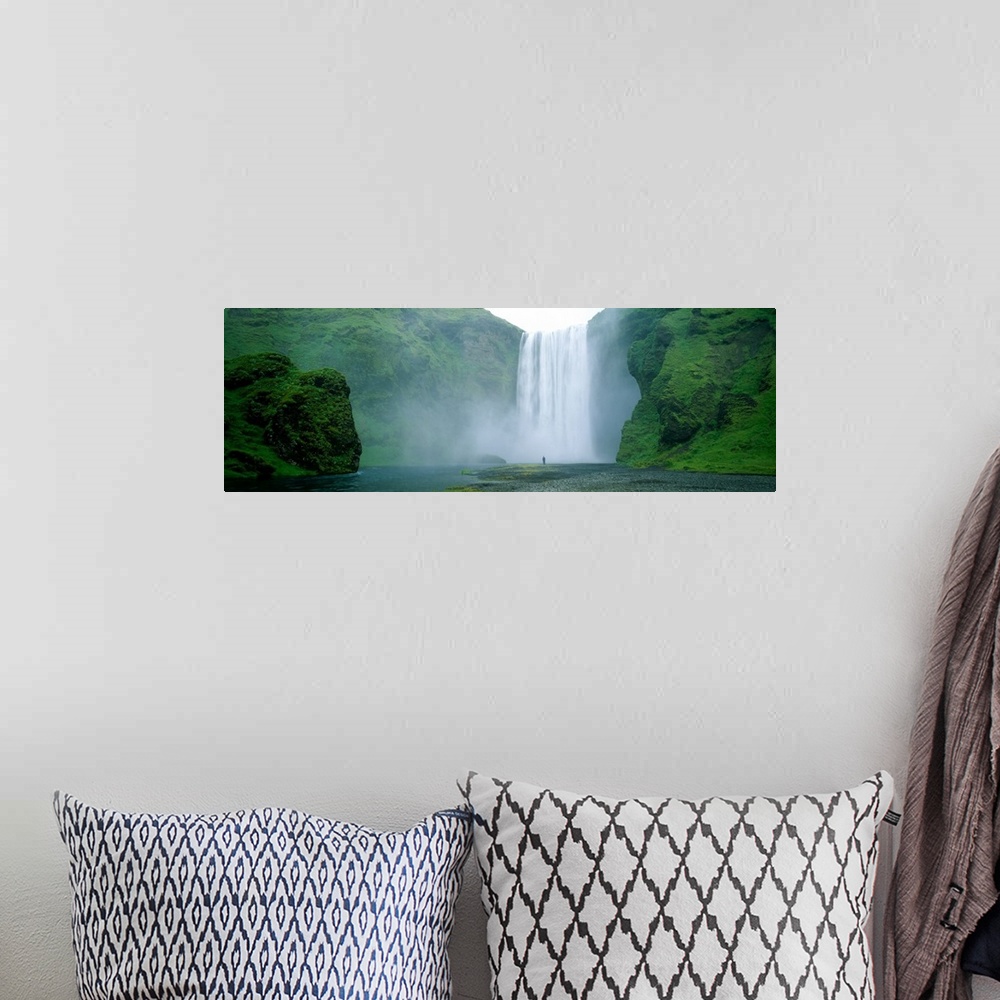 A bohemian room featuring Panoramic photo of a wide waterfall spilling over a cliff into the water below with a man standin...
