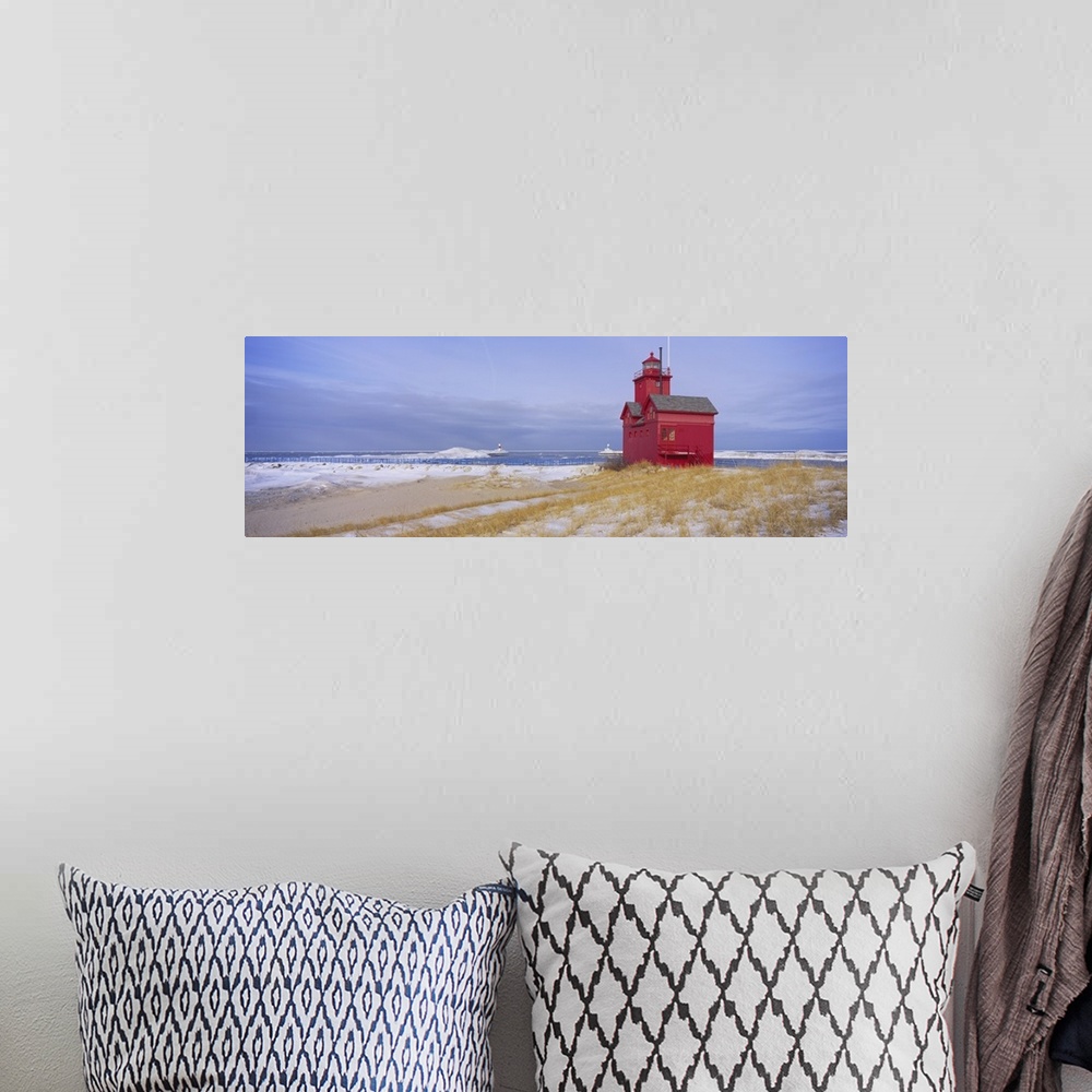A bohemian room featuring Lonely red light house on the edge of the water on a snowy beach, standing out against the pale c...