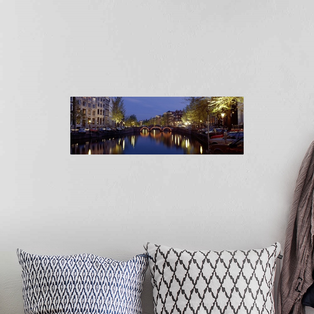A bohemian room featuring A wide angle view of a canal in Amsterdam with buildings and street lights illuminated on either ...