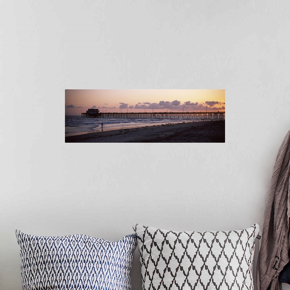 A bohemian room featuring A beach board walk extends out into the ocean in this landscape photograph of the sun setting on ...