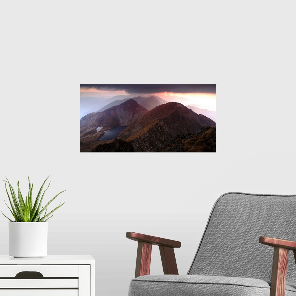 A modern room featuring Sunset just visible under dark clouds over the Fagaras Mountains in Romania.